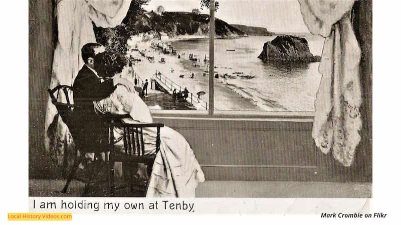 Old postcard of a couple gazing out the window at Tenby's beach